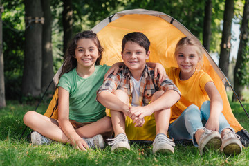 happy boy sitting with cute friends near camp