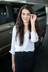 Female car dealer standing in showroom near new car