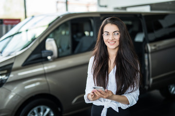 Young beauty woman dealer use phone while standing in cars showroom