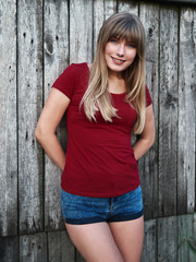 Lifestyle happy blonde woman dressed red blouse blue denim jeans shorts emotionally posing leaning wooden fence european cozy village in evening twilight