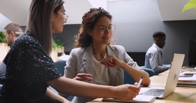 Friendly diverse female colleagues discussing online project at workplace