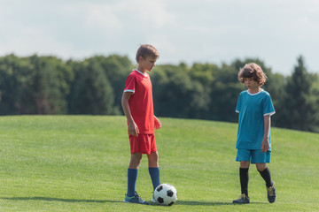 Obraz na płótnie Canvas cute curly boy playing football with friend on grass in park