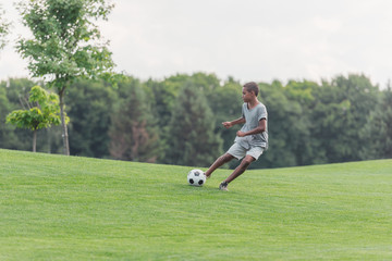 cute african american boy playing football on green grass