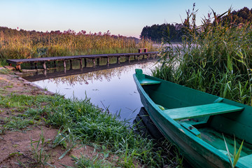 Obraz premium old wooden boat in the reed bushes on the bank of wide river or lake