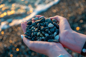 Girl holds a handful of green pebbles. Against the background of the sea.