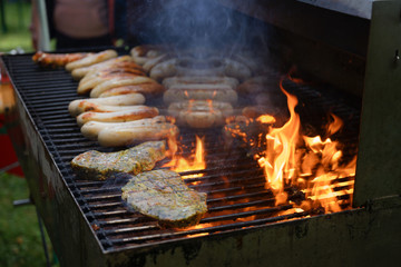 meat and sausage are roasted on a large charcoal grill