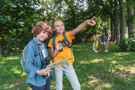 Selective Focus Of Happy Kid With Binoculars Pointing With Finger Near Friend Holding Map