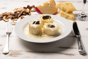 Homemade rondelli with four cheese and mushuroom sauce in white plate on rustic white wooden table background, soft light