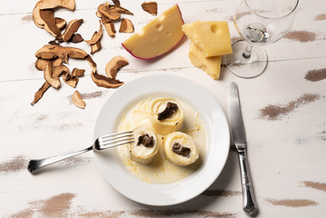 Homemade rondelli with four cheese and mushuroom sauce in white plate on rustic white wooden table background, soft light