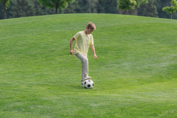 cute boy playing football on green grass