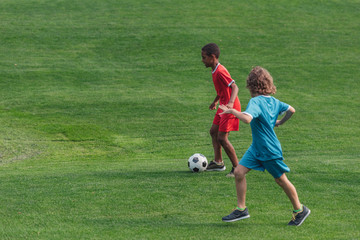 Naklejka premium cute multicultural kids playing football on grass