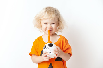 Happy Halloween. curly funny girl child in a pumpkin costume drinks a cocktail from a skull on a white background
