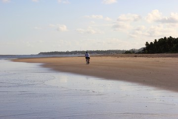 Fototapeta na wymiar A man alone riding a bike on the beach. Sand and water in the wide beach.