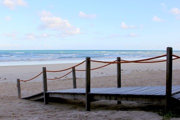Wooden sidewalk leading to the beach sand. In front the sea and blue sky in the horizon.