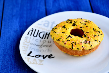 A delicious donut on a white plate, on a table of painted blue boards.