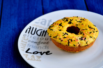 A delicious donut on a white plate, on a table of painted blue boards.