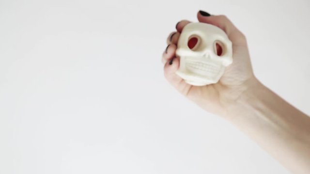 female caucasian hand with black nails holds and squeezes an antistress skull on a white background. halloween concept