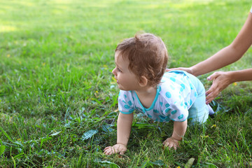 Cute little baby with mother crawling on green grass in park, space for text
