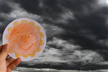 man holding picture of a smiling sun against dark and horrified clouds concept of faith and optimism