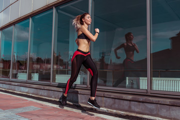 Beautiful girl runs in the summer in the city against the background of glass windows of the building, healthy and stylish active lifestyle, fitness motivation workout. Free space for text.