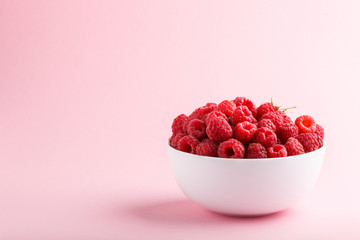 Fresh raspberry in white bowl on pink pastel background. side view.