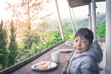 Smiling Asian boy is eating breakfast on a beautiful natural background