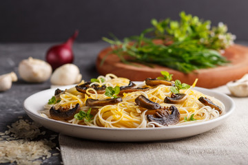 Rice noodles with champignons mushrooms, egg sauce and oregano on a black concrete background. side view, close up.