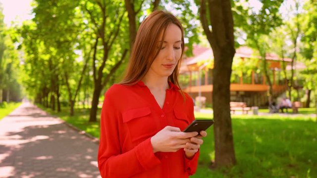 elegant woman standing on the street holding smart phone typing message or checking email summer sunlight outdoors background