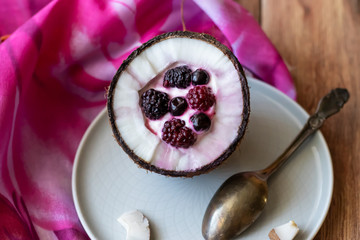 Berry dessert with yogurt in a cup of coconut on a wooden background. Blackberries, raspberries, blueberries, black currants.