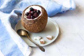 Berry dessert with yogurt in a cup of coconut on a light background. Blackberries, raspberries, blueberries, black currants. Blue napkin