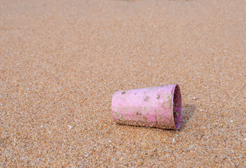 single use plastic pink cup littering on the beach with sand blurred background, close up