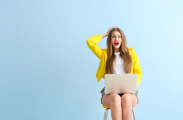 Excited young woman with laptop  sitting on chair against color background