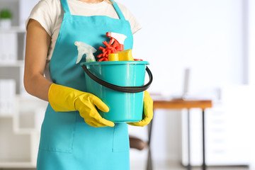 Female janitor with set of cleaning supplies in office