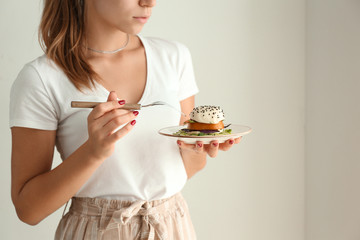 Young woman eating tasty salad on light background