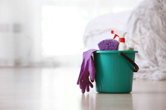 Bucket with cleaning supplies on floor in room - a green bucket with a purple glove and a purple rag