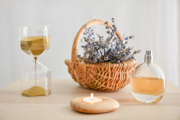 Obraz na płótnie Canvas Burning candle with bottle of perfume, basket with lavender and hourglasses on table
