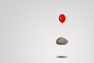 Business Success Concept : Red balloon tied to heavy rocks floating over floor.