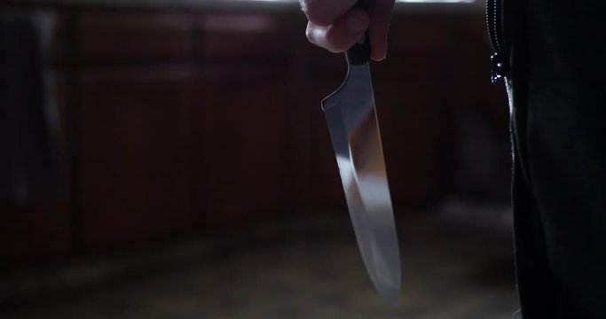 A scary slasher killer holding a kitchen knife and walking towards his murder victim in their home.