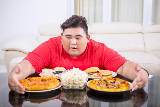 Obese man embracing lots of unhealthy food
