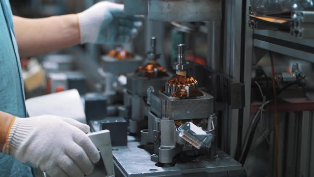 Industrial worker assembling electrical motor on automatical equipment at factory