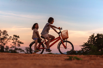 Obraz premium two children playing riding bike on mountain at sunset sky background