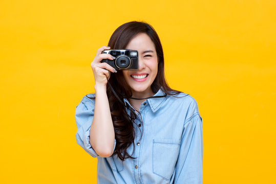 Young Asian woman photographer smiling and taking picture on yellow studio background