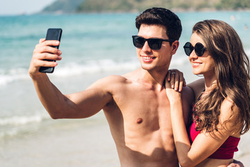Romantic lovers young couple relaxing together on the tropical beach.Man and woman taking selfie with smartphone and enjoy life.Summer vacations