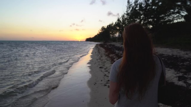 Red headed woman taking a photo on her iPhone on a tropical beach