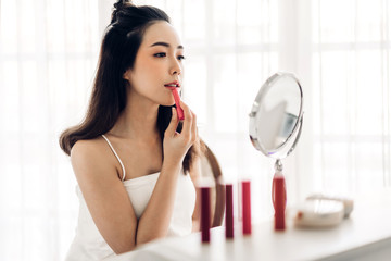 Smiling beautiful woman fresh healthy skin looking on mirror and enjoying applying lips with red lipstick at home.facial beauty and cosmetic concept