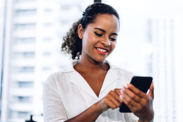 Smiling beautiful professional business african american black woman working and using smartphone standing in office