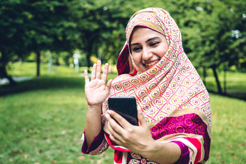 Portrait of happy arabic muslim woman with hijab dress smiling using and talking on the smartphone in summer park