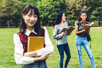 Smiling woman international students or teenagers standing and holding book smiling at camera with group of students in park at university.Education and friendship Concept