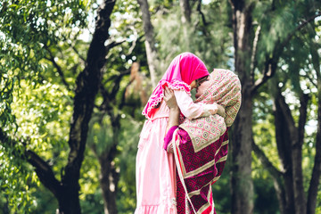 Portrait of happy lovely family arabic muslim mother and little muslim girls child with hijab dress smiling and having fun hugging and kissing together in summer park