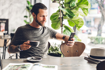 Handsome bearded hipster man use smartphone with coffee at table in cafe.Communication and...